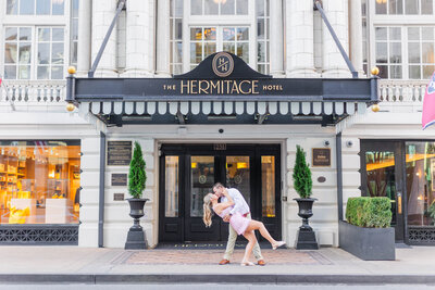 A stunning portrait in front of the state capitol building of an engaged couple wearing a light pink satin dress and a white button up with khaki pants. The groom is dipping his bride and kissing her. Shot by Nashville wedding photographer, Brooke Elliott
