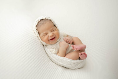 adorable newborn girl smiling as she dreams in her handmade bonnet from oklahoma city