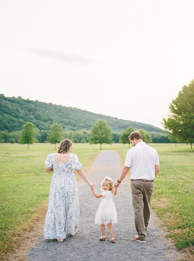 Mother, newborn baby, toddler sister, and father walk away from camera down a path, while toddler sister looks back toward photographer Little Rock Bailey Feeler