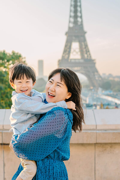 Mother holding her young son as they smile at the camera with the Eiffel Tower in the background at Trocadéro during a Paris family photoshoot.