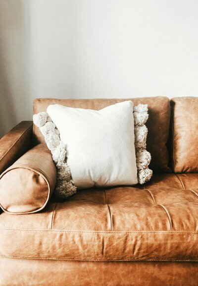 A white textured pillow on a brown leather couch.