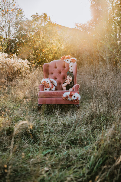 Milestone photo of baby girl in pink chair with flowers on it in a field.