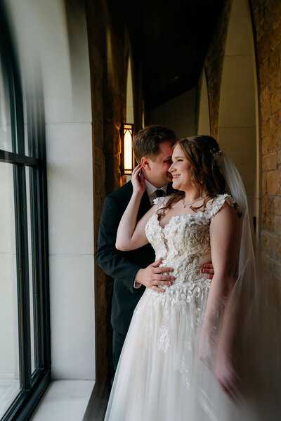 Groom hugging smiling bride near arched window