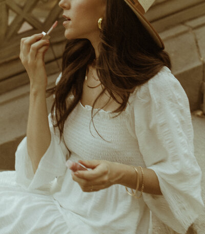 Closeup shot of woman in a white summery dress putting on lipgloss