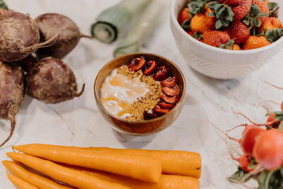 Yogurt, granola and fruit bowl on the counter next to a bowl of strawberries