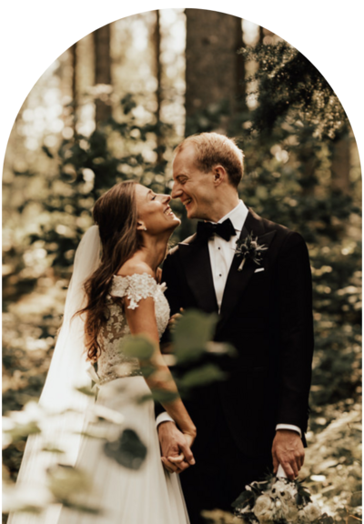 brud håller i brudgummens hand och tittar upp mot honom och ler under bröllopsfotografering i skogen i enköping