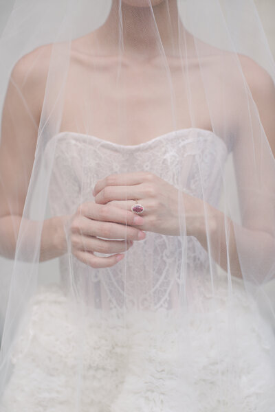 A close up of a bride's hands under her veil with a ruby engagement ring