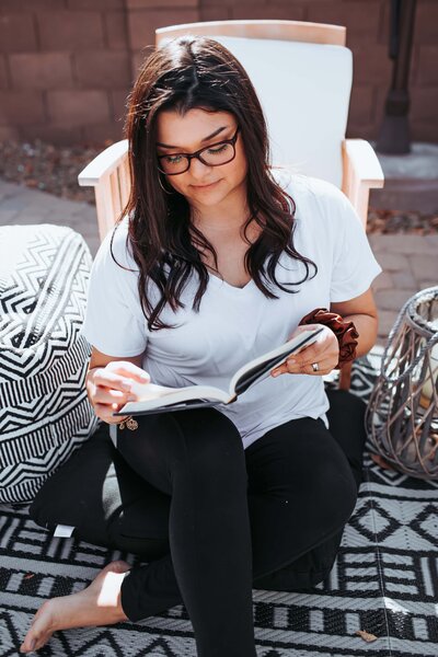 woman with glasses reading on a couch outside