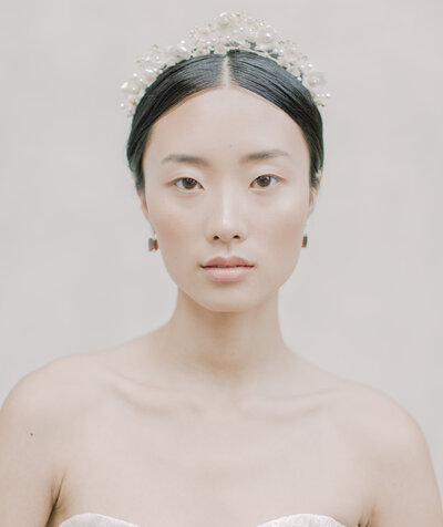 A beautiful bride with black hair and a pearl crown looks directly at the camera