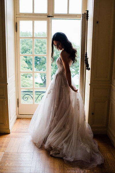 bride adjusting wedding dress in window