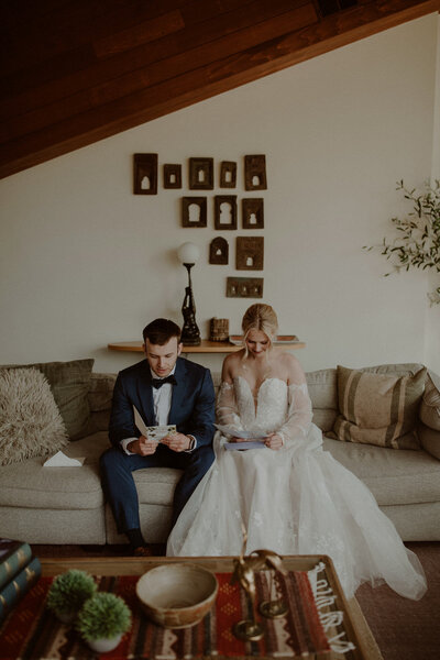 Bride and groom read letters sitting on the couch together