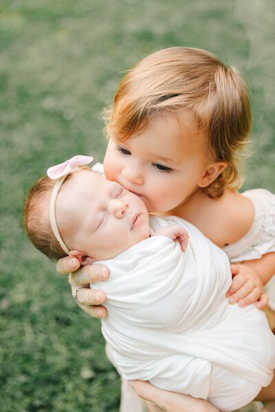 toddler sister kisses newborn baby girl during newborn photography session with Asheville Newborn Photographer Rachel Marie Photography at the UNCA Botanical Gardens