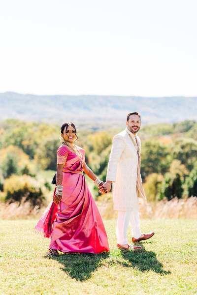 bride and groom walking in a field while holding hands