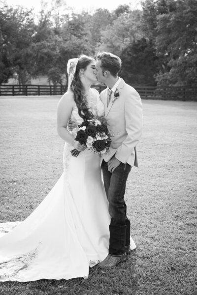 Austin-based wedding photographer captures a timeless black and white photo of a bride and groom kissing in a field.