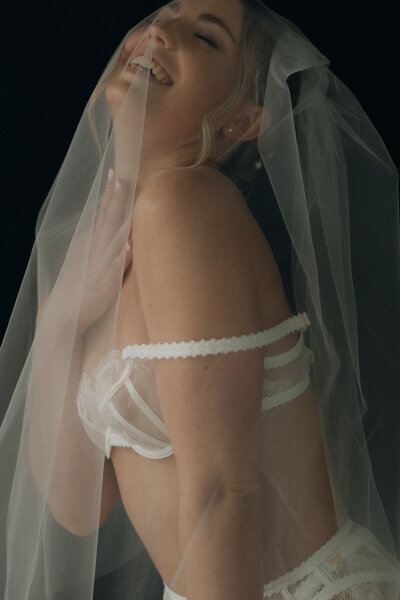 Woman in white lingerie and a veil in front of a black background