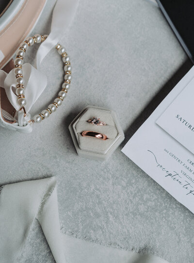 Close-up of a diamond engagement ring in front of a bouquet of white roses and greenery, placed on a stone surface. The background is softly blurred, highlighting the details of the flowers and ring. Taken at the Chrysler Museum in Norfolk, Virginia. Shot by Quinn Photography LLC.