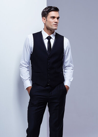 Handsome man in studio wearing black vest, white shirt, black pants and black tie..