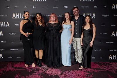 Group of six individuals of the Blake & Kwan Team dressed elegantly in formal attire at an AHIA award event with a branded backdrop.