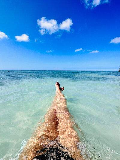 A traveler’s legs submerged in the crystal-clear turquoise ocean, capturing a peaceful and serene honeymoon moment in a tropical destination.