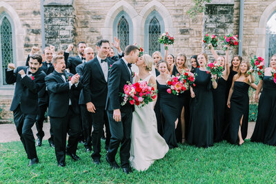 Bridal party dressed in all black cheering while bride and groom kiss