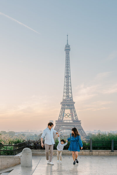 Family of four — mother, father, young boy, and baby — walking near the Eiffel Tower at Trocadéro, with the mother holding the baby during a Paris family photoshoot.