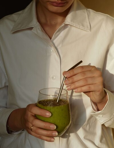 A woman wearing a white blouse holding a green smoothie