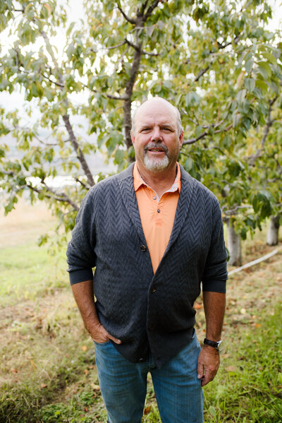 A smiling man standing next to an apple tree in the Wenatchee Valley.