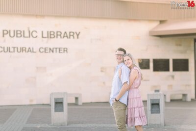 Groom to be is embraced from behind by his Bride during an engagement session at the the Huntington Beach Public Library