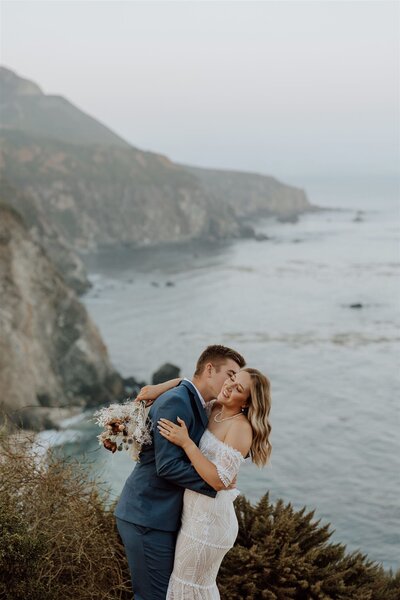 bride and groom embracing on a cliff overlooking the ocean