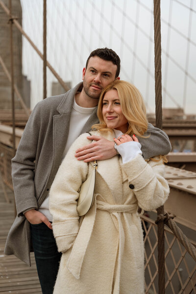 a man and woman on the Brooklyn bridge looking into the distance 