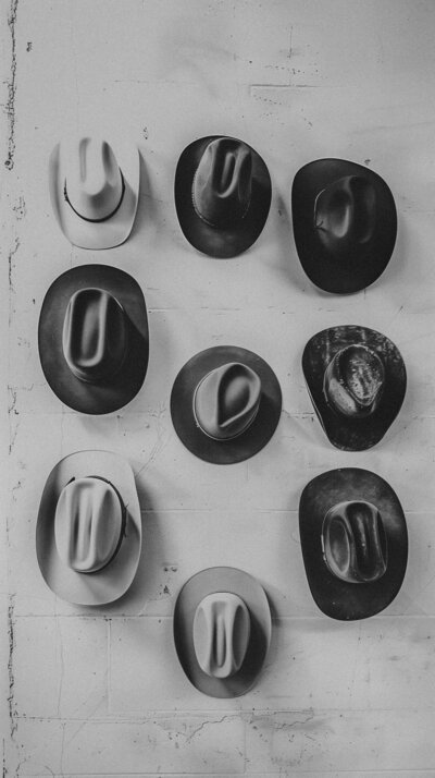 Nine cowboy hats, of various styles and conditions, hanging on a white wall in a 3x3 grid arrangement, make for an intriguing visual—a unique take on brand identity inspired by Sweet Pea Ink Creative.