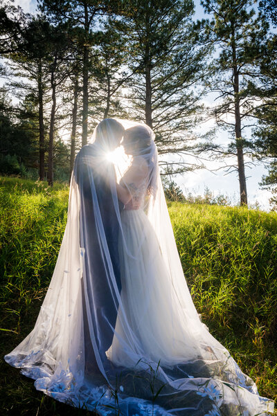 A bride and groom snuggle under the bride's veil at golden hour.