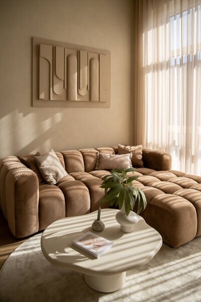 Sfeervolle zithoek in Studio Laurant met een organische sofa, twee handgemaakte kunstwerken en een spiegel, voor een elegante en artistieke uitstraling.