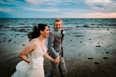 a photo of a bride and groom running on the beach in cape cod massachusetts
