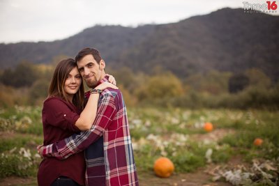 Engaged couple embrace as they pose for photos in the pumpkin patch in Riley's Farm