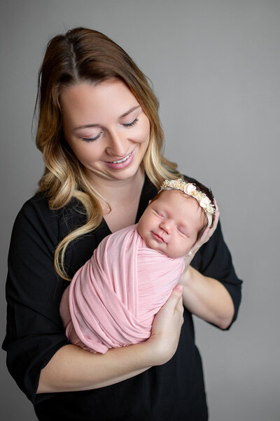 Blonde mother dressed in black holding baby girl wrapped in soft pink while mother looks at baby