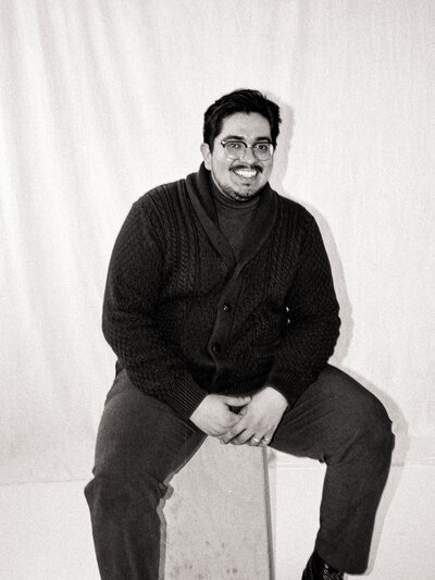 Black and white film portrait of Javi, seated and smiling at the camera — co-founder and cinematographer at Castillo Holliday Photo + Film.