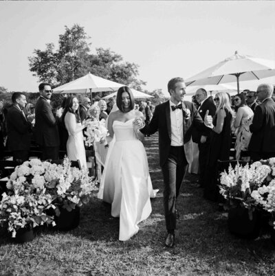 A bride and groom joyfully walk down the aisle together at their wedding ceremony, surrounded by floral decorations.