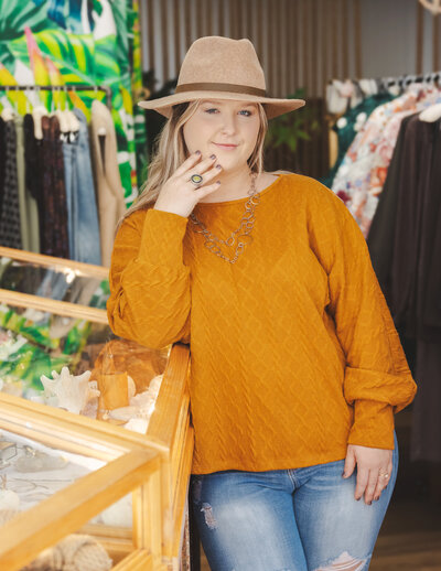 Boutique model wearing yellow sweater, jeans, and coordinated hat modeling jewelry