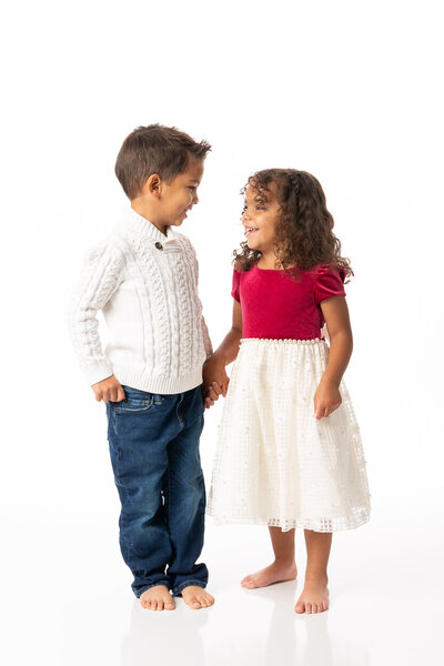 toddler siblings dressed in holiday best, holding hands and smiling at each other like they are up to something, adorable queen city kids 2024