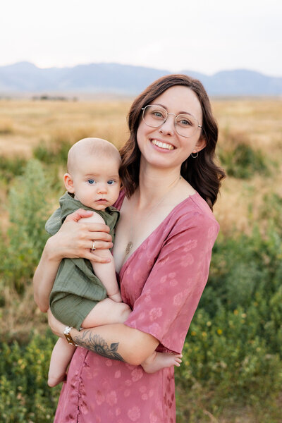 A mom holds her young baby boy and they both look a the camera.