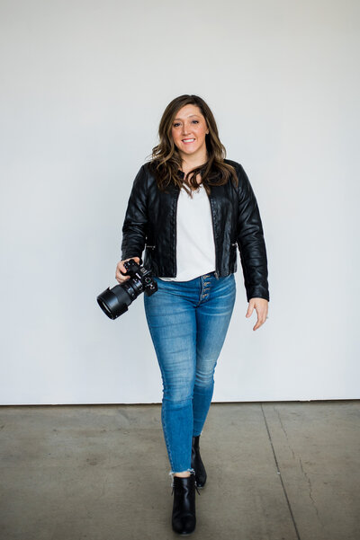 Colorado photographer, Sarah Mcnew, smiles at the camera in a summery, green setting.