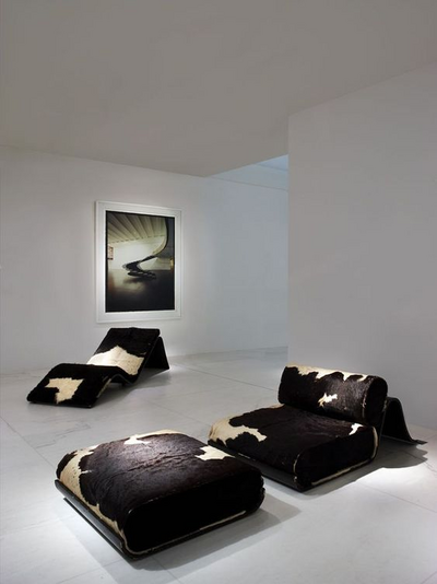 A minimalist modern lounge with sleek black cushions and cowhide patterns, under a framed piece of art