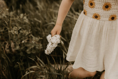 Photo of a little girl holding a flower in the tall grass.