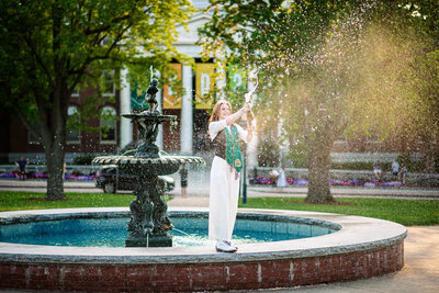 A young woman sprays champagne in front of the University of Vermont fountain in Burlington, Vermont, celebrating with energy and joy