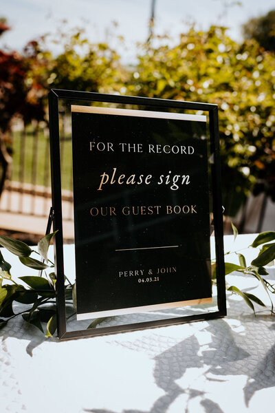 Black and gold guest book sign in a stylish black frame at a spring wedding at the Palm Event Center in Pleasanton, CA.