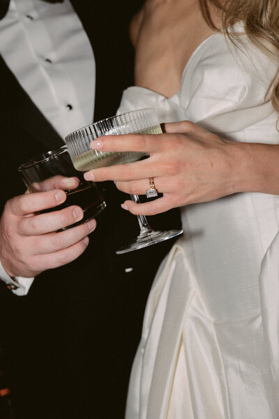 Romantic wedding portrait with couple holding hands showcasing their rings and wedding attire.