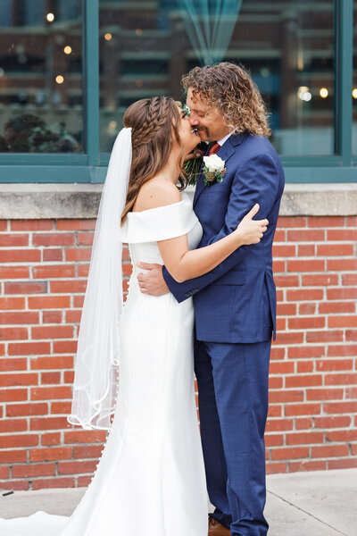 Couple leaning in for a kiss during wedding day in front of brick building