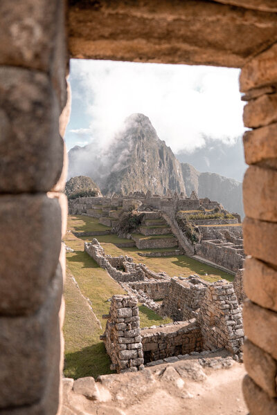 A view through a stone doorway overlooking the ancient ruins of Machu Picchu with mist-covered mountains in the background.