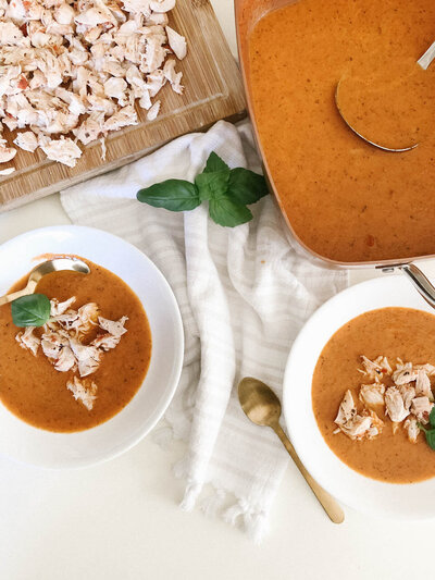 Flat lay image of bowls of tomato soup and ingredients on the counter